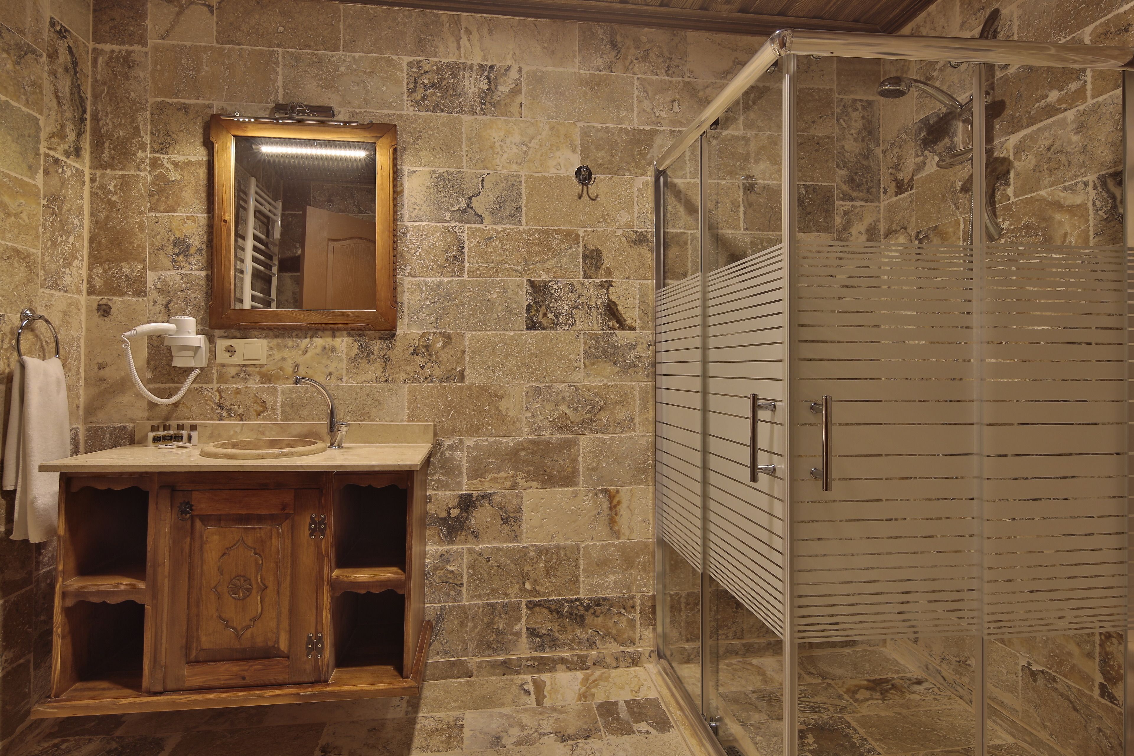 A bathroom with a stone wall, wooden vanity, and a glass shower enclosure.
