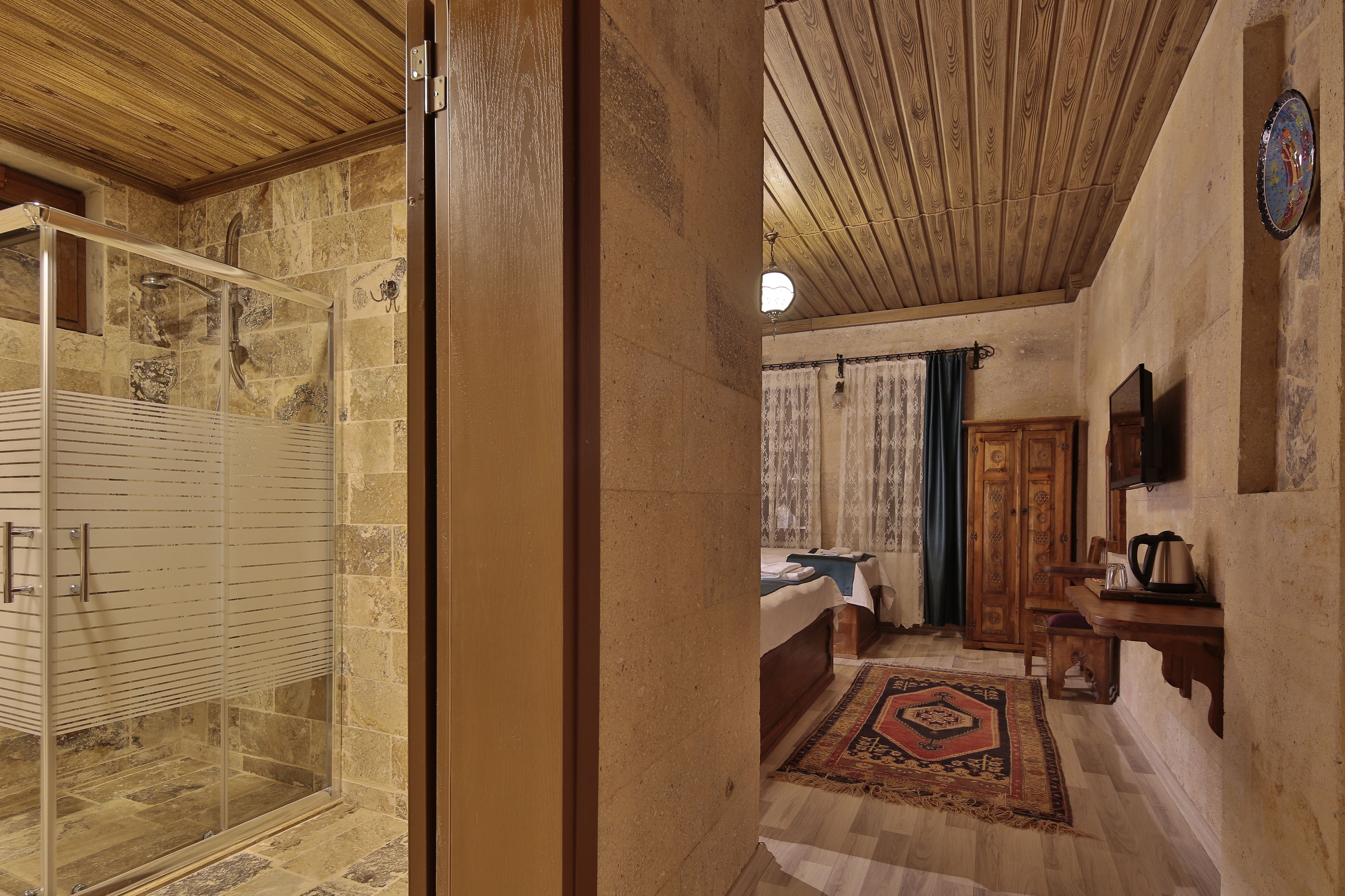 A room with a shower, a bed, a wooden ceiling, and a stone wall.