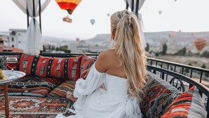 Una persona sentada en un sofá estampado, vestida con un vestido blanco, bajo un dosel con un farol colgante.