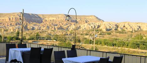 A terrace with tables and chairs, a lamp, and a view of a mountainous landscape.