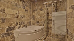 Un baño con una bañera independiente, cabina de ducha con vidrio y paredes de baldosas de piedra.