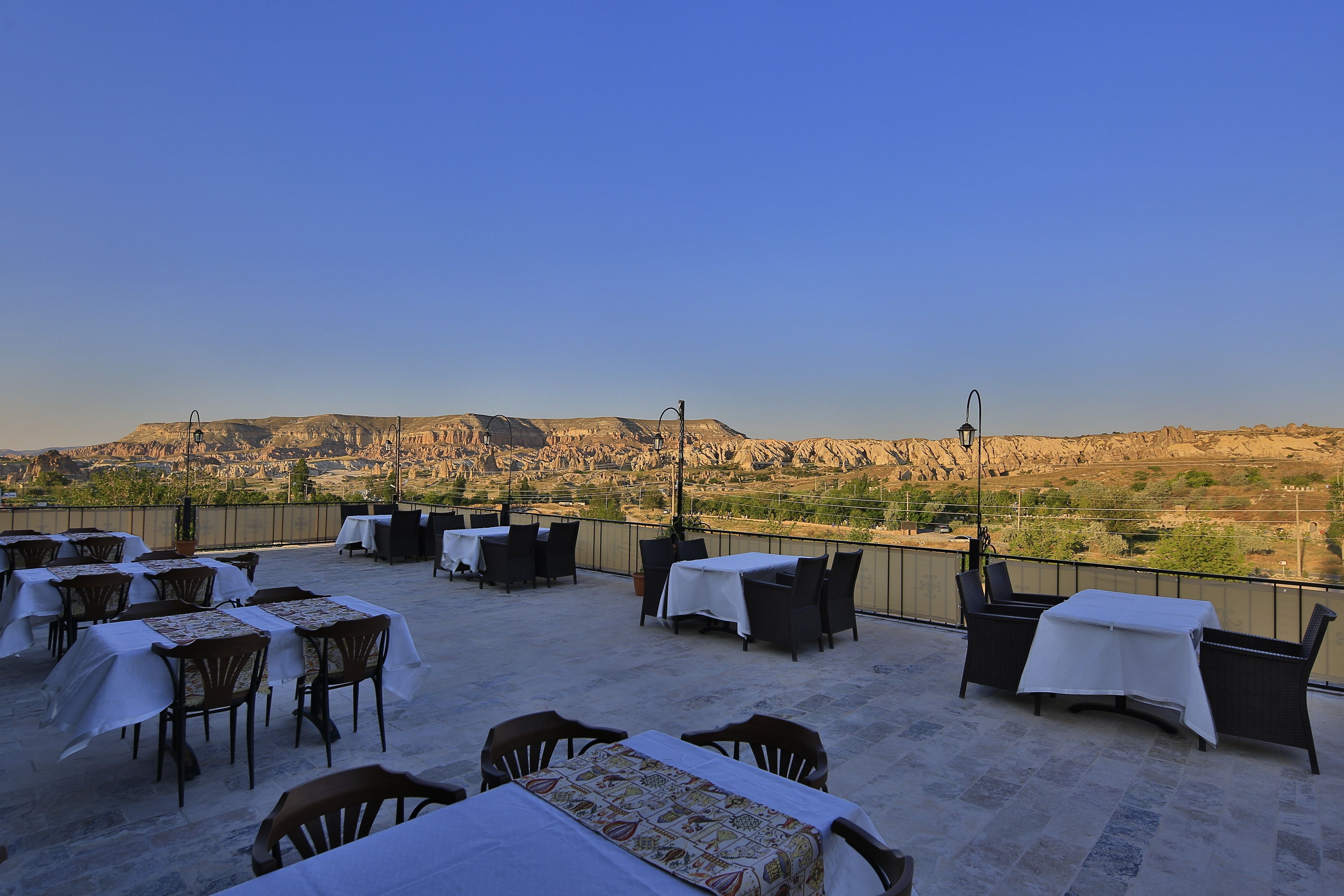 A rooftop terrace with tables and chairs, offering a view of a mountainous landscape.