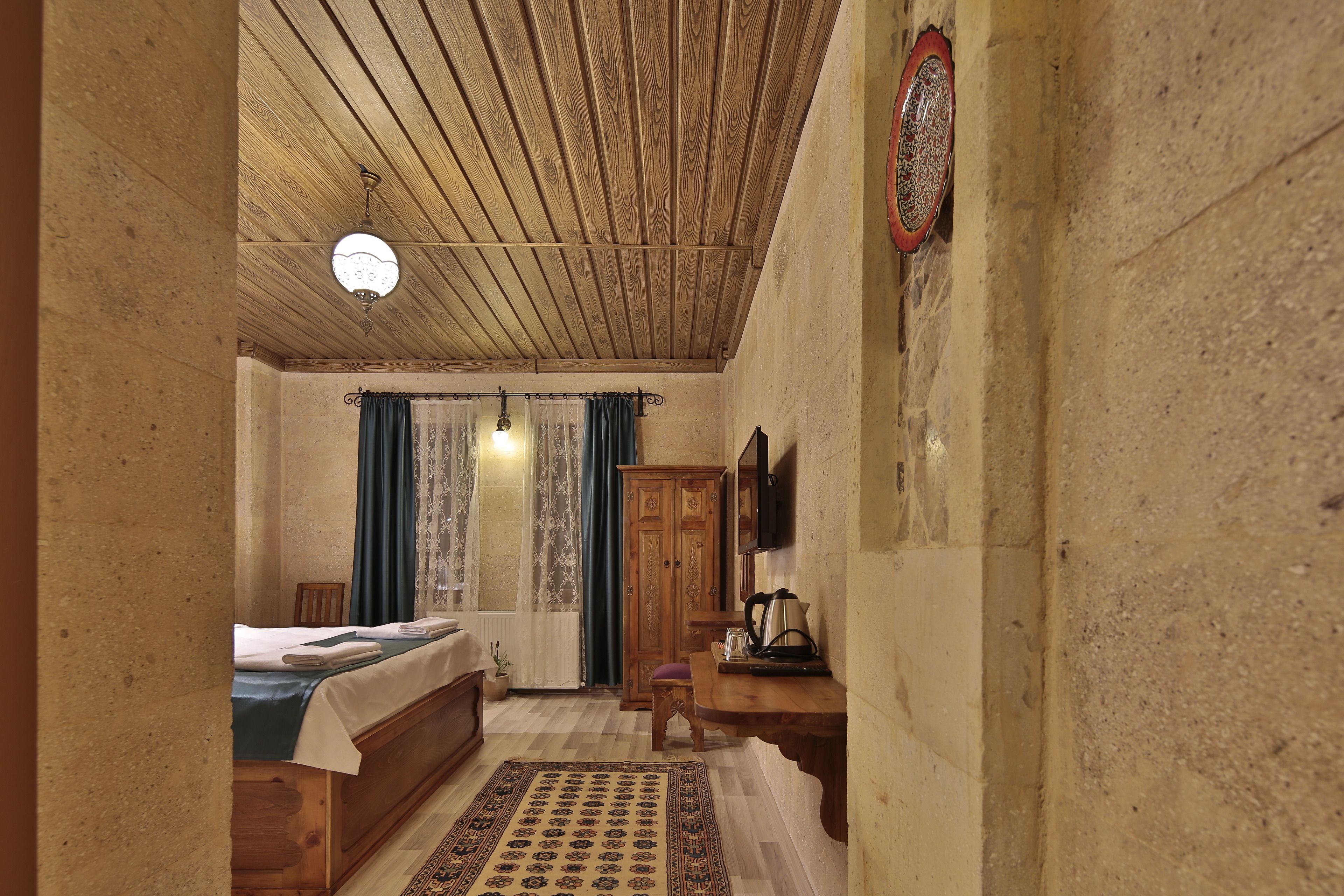 A cozy room with a wooden ceiling, a bed with a blue bedspread, a wooden desk, and a patterned rug.