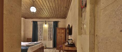 A cozy room with a wooden ceiling, a bed with a blue bedspread, a wooden desk, and a patterned rug.