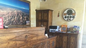 Un mostrador de recepción de madera con un cuadro grande de un paisaje montañoso, un reloj y una alfombra estampada.