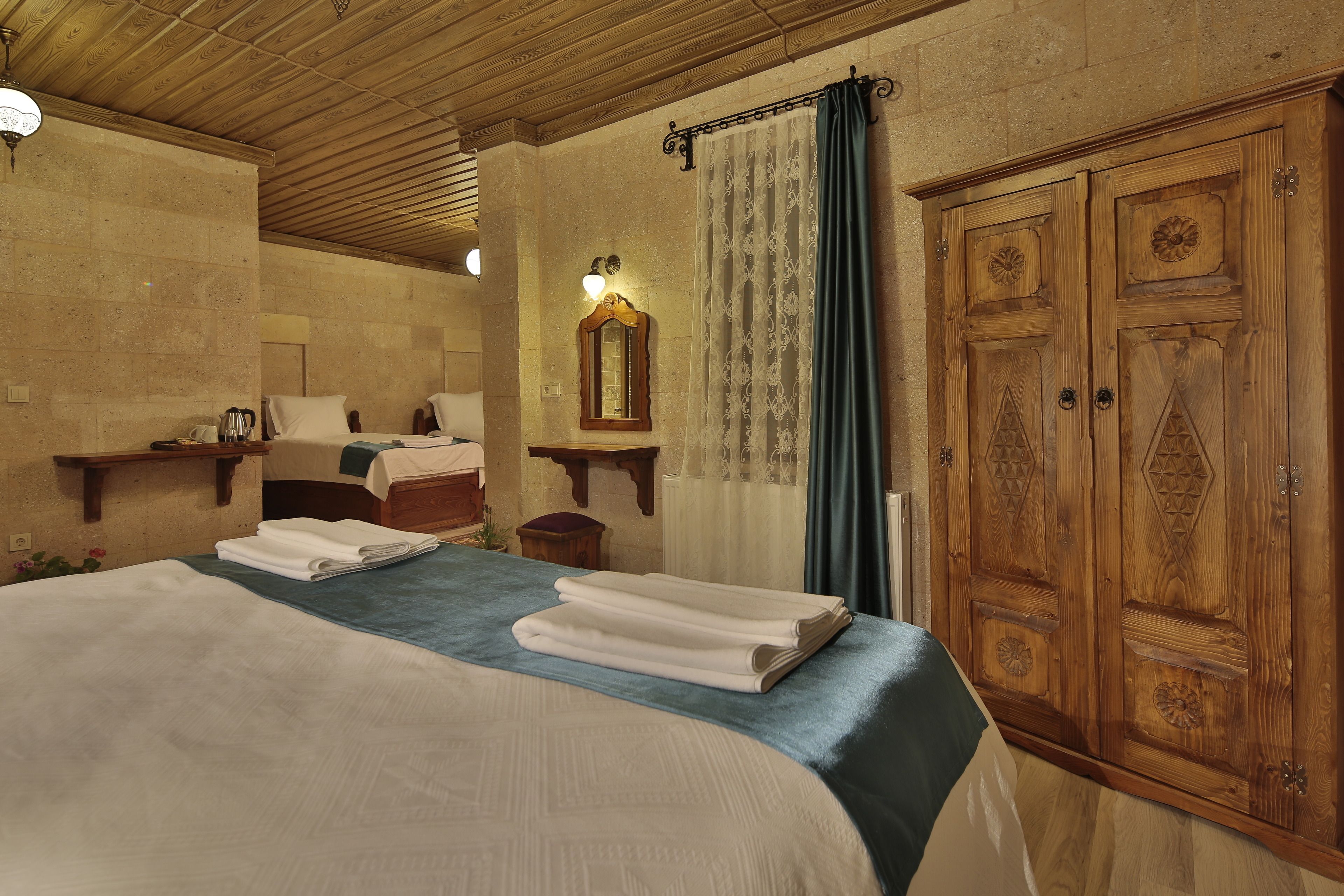A hotel room with a large bed, a wooden wardrobe, a nightstand, and a mirror.