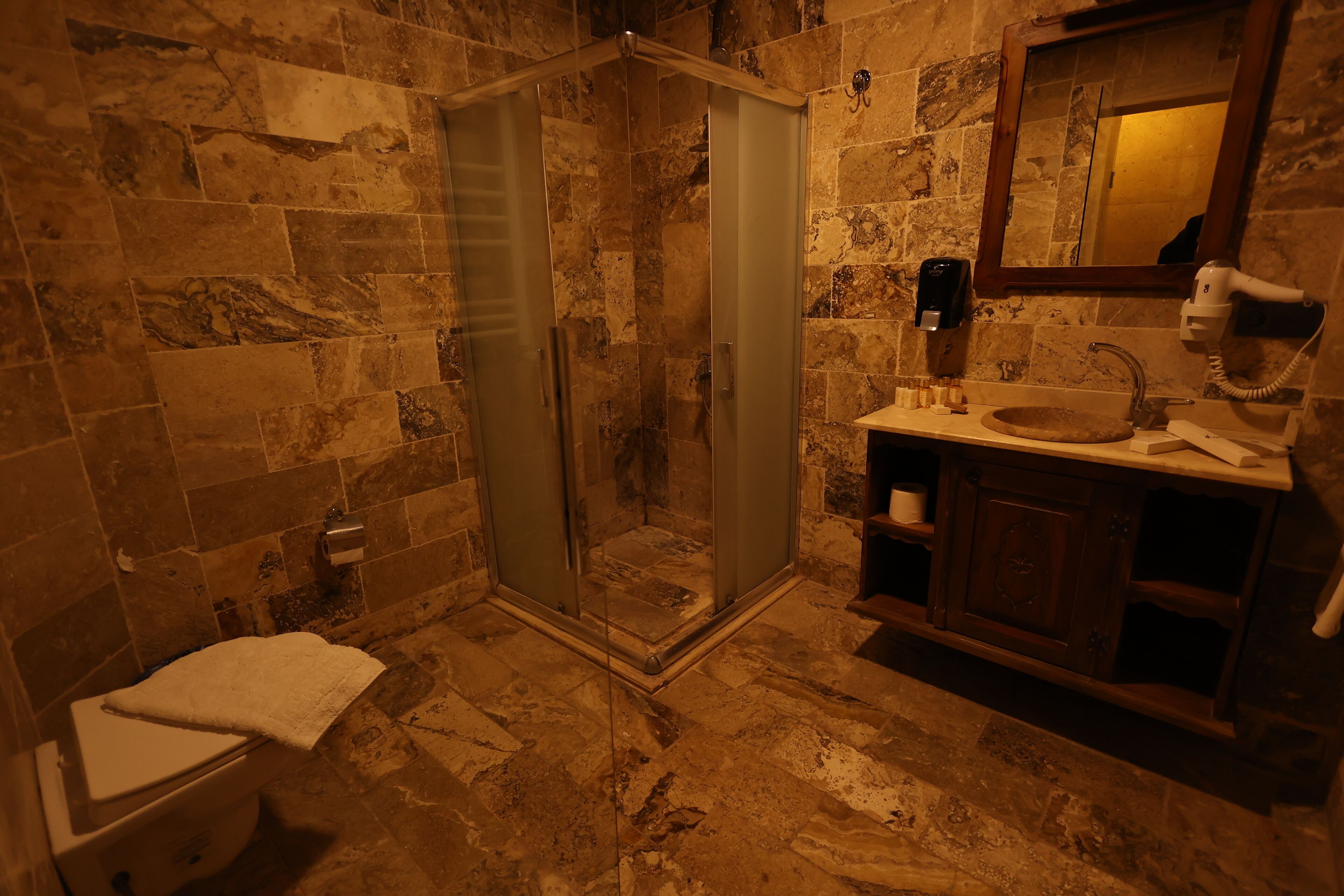 Un baño con ducha de vidrio, pared de azulejos de mármol, tocador de madera y un espejo.