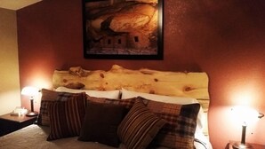Un dormitori amb un llit gran, dues taules de nit amb làmpades i un quadre amb una cova a la paret.