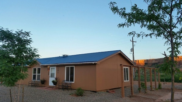 A single-story house with a blue roof, a front porch with chairs, and a small garden area.