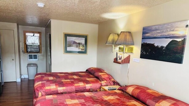 Una habitación con una cama, una mesita, una lámpara, un cuadro en la pared y una ventana.