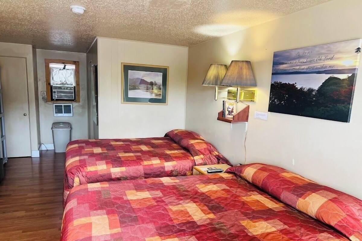 Una habitación con una cama, una mesita, una lámpara, un cuadro en la pared y una ventana.