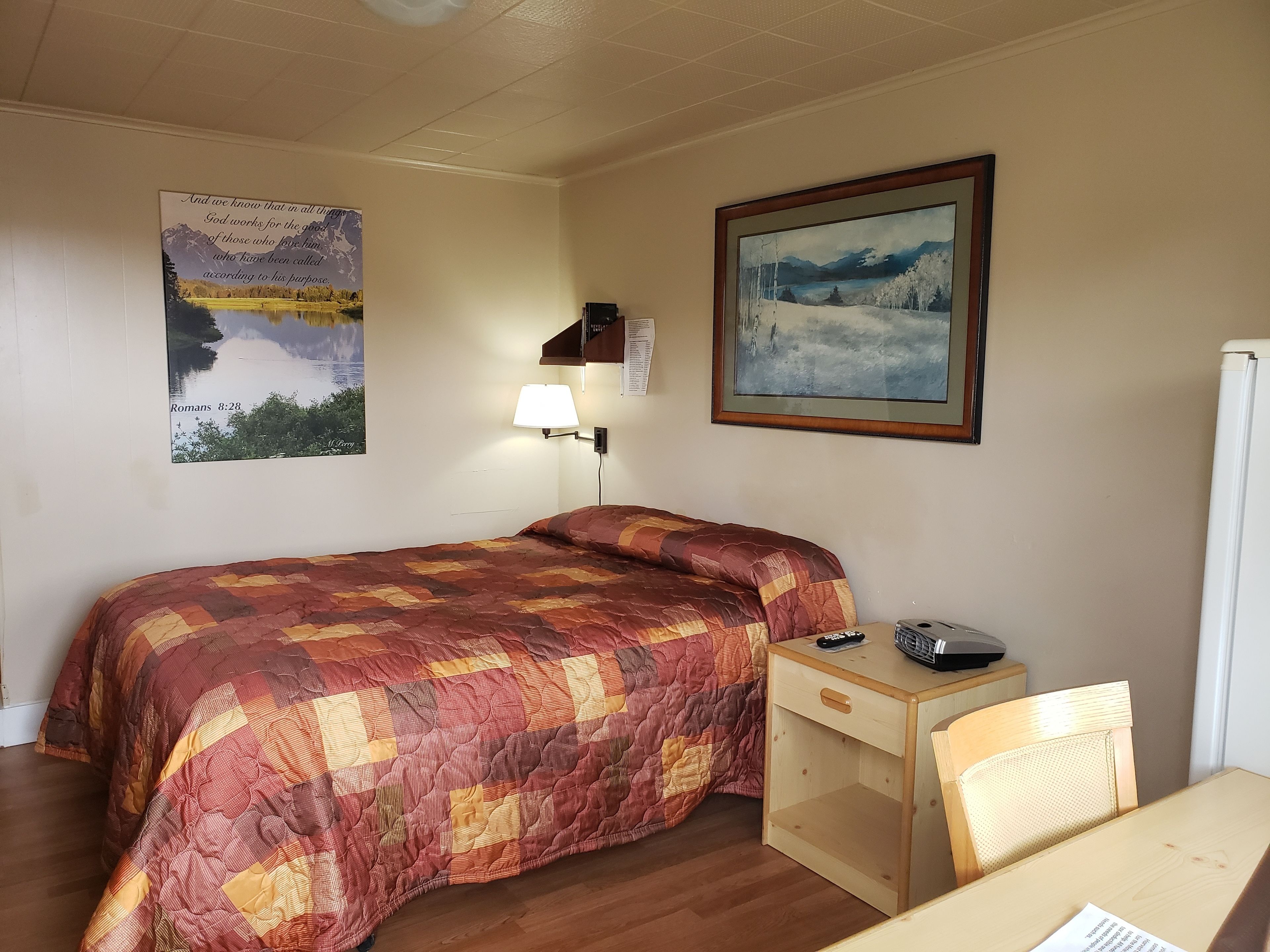 Une chambre à coucher avec un lit, un bureau, une chaise, une lampe et deux tableaux encadrés accrochés au mur.