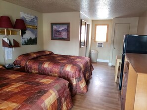 A room with two beds, a desk, a TV, and a window.