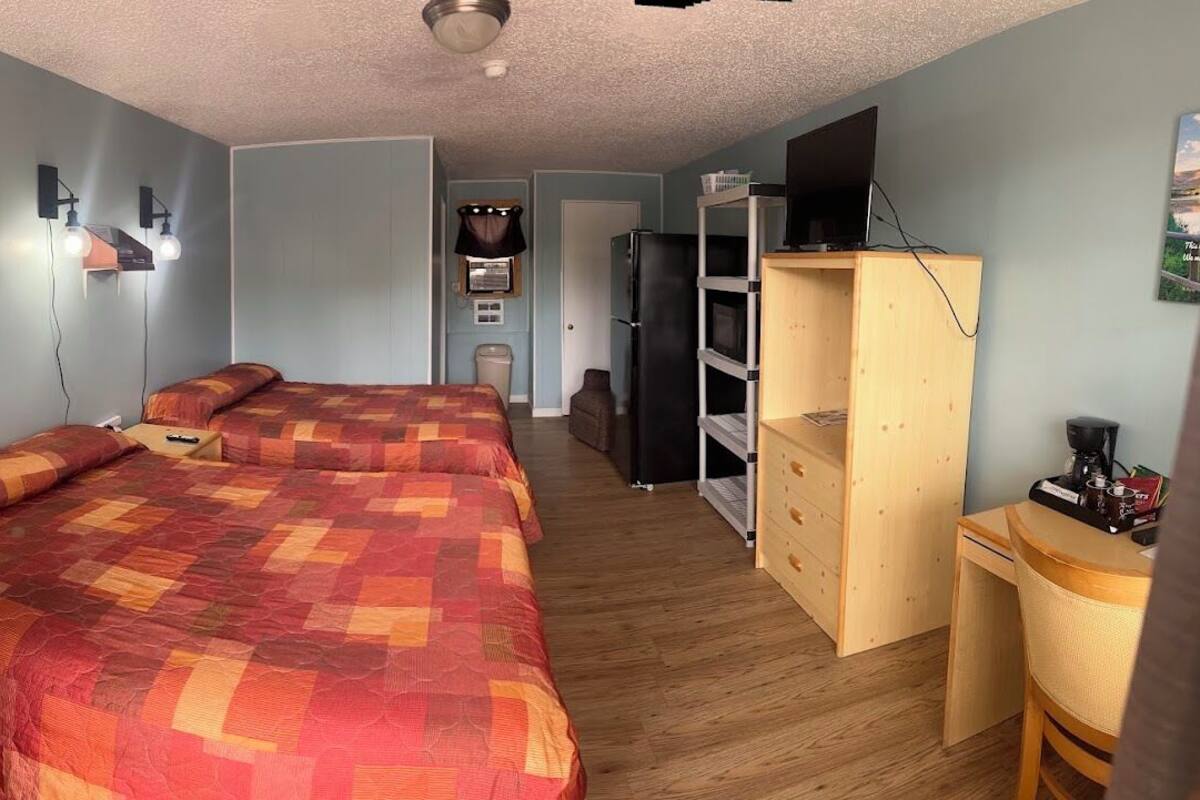 Una habitación con dos camas, un escritorio de madera, una estantería y un refrigerador.