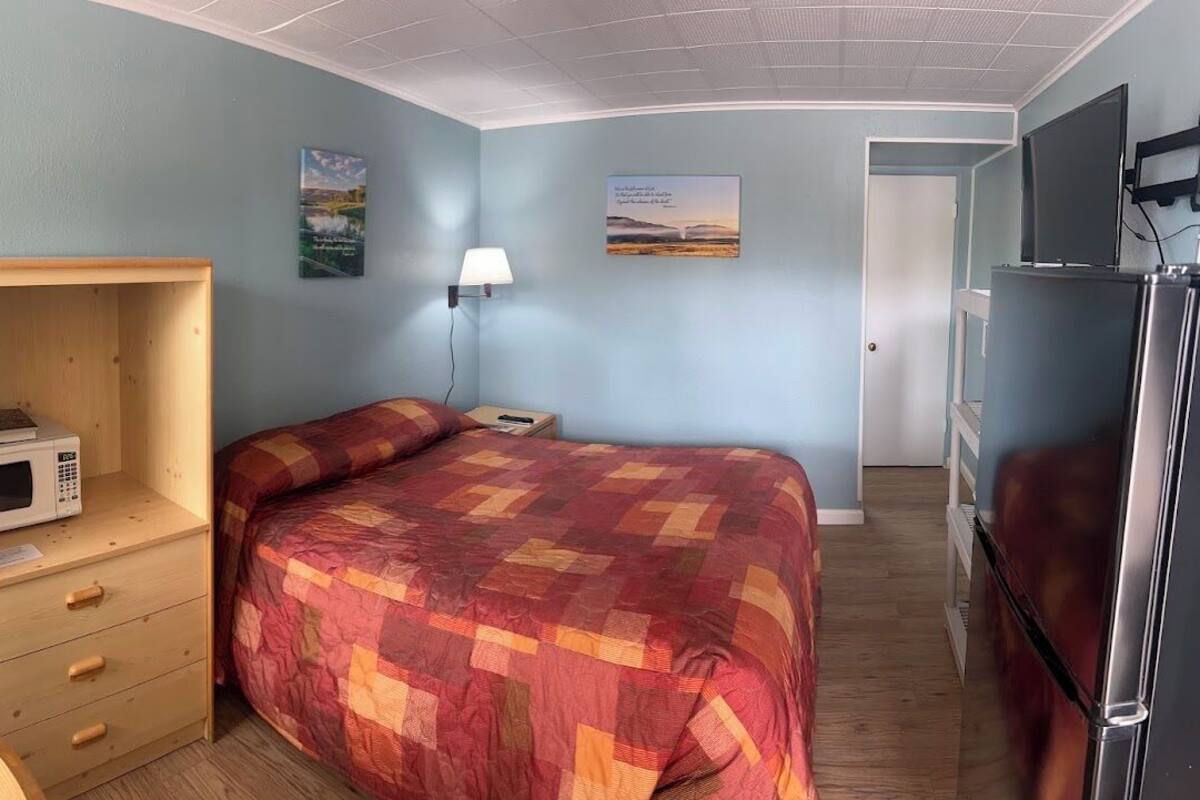Un dormitorio con una cama, una mesita de noche de madera con microondas, una lámpara y un televisor.
