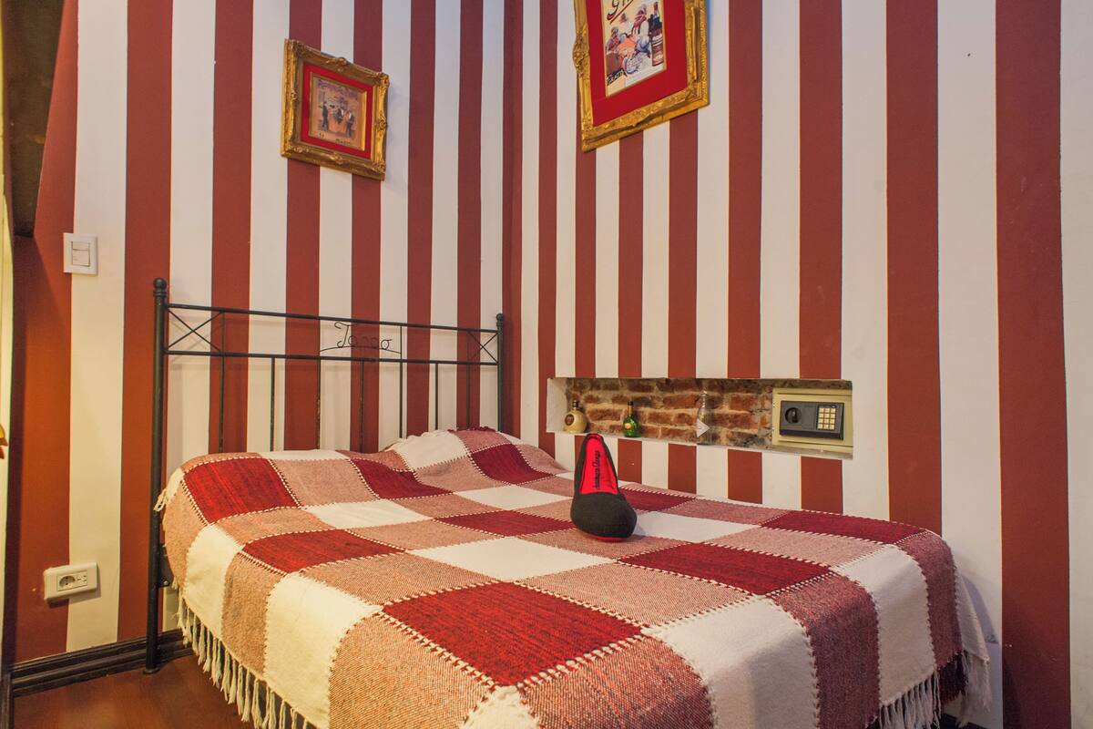 A bed with a checkered blanket, a black headboard, and a wall-mounted alarm clock.