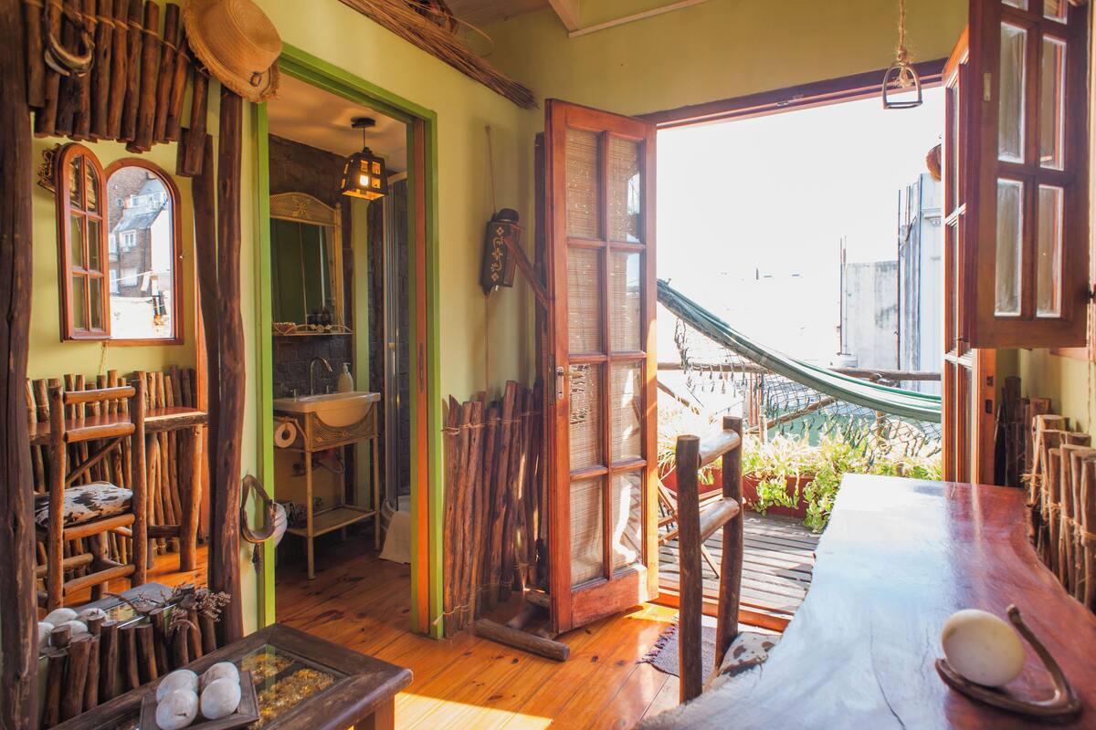 A rustic room with wooden furniture, a large wooden table, and a view of a garden through an open door.