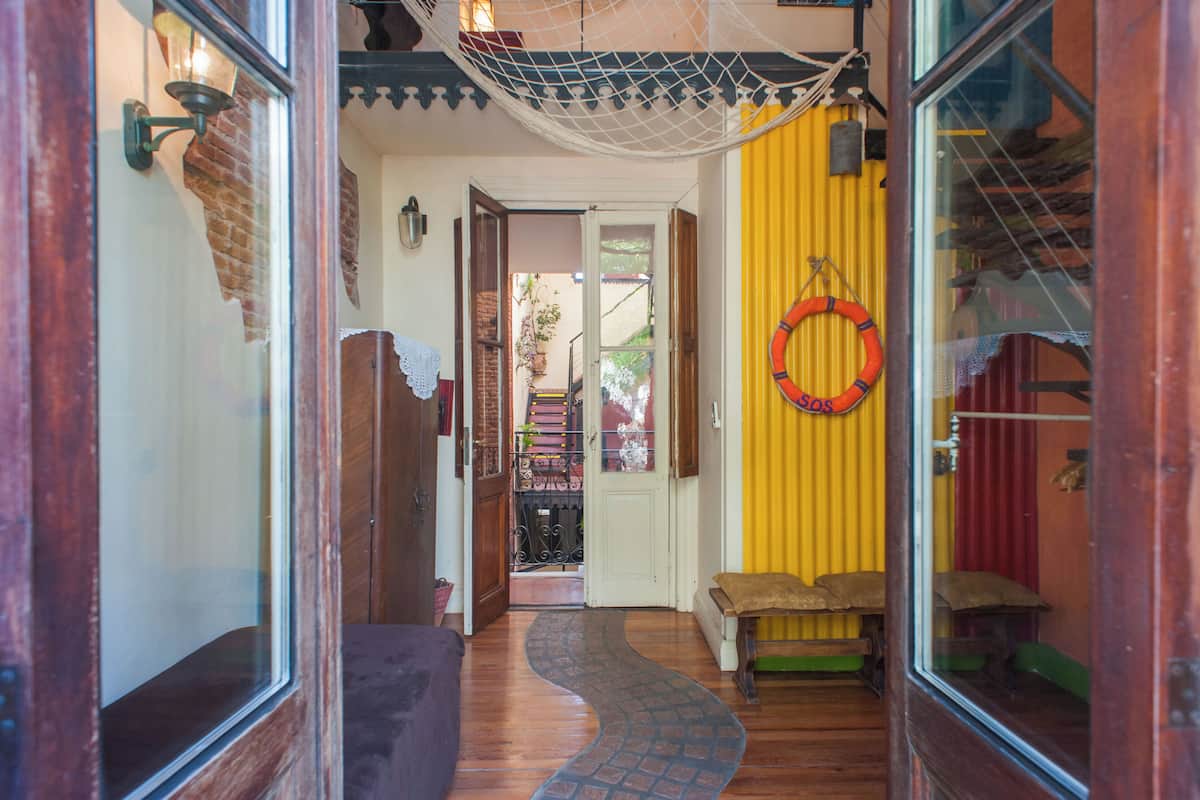 A narrow hallway with a wooden floor, a bench, a hammock, and a yellow wall with a red circular decoration.