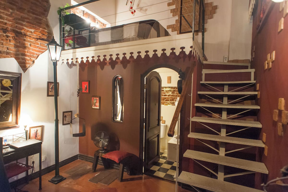 A room with a loft area, a staircase, and a small seating area.