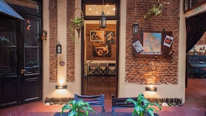 Una entrada acogedora con pared de ladrillo, plantas colgantes y una mesa con sillas.