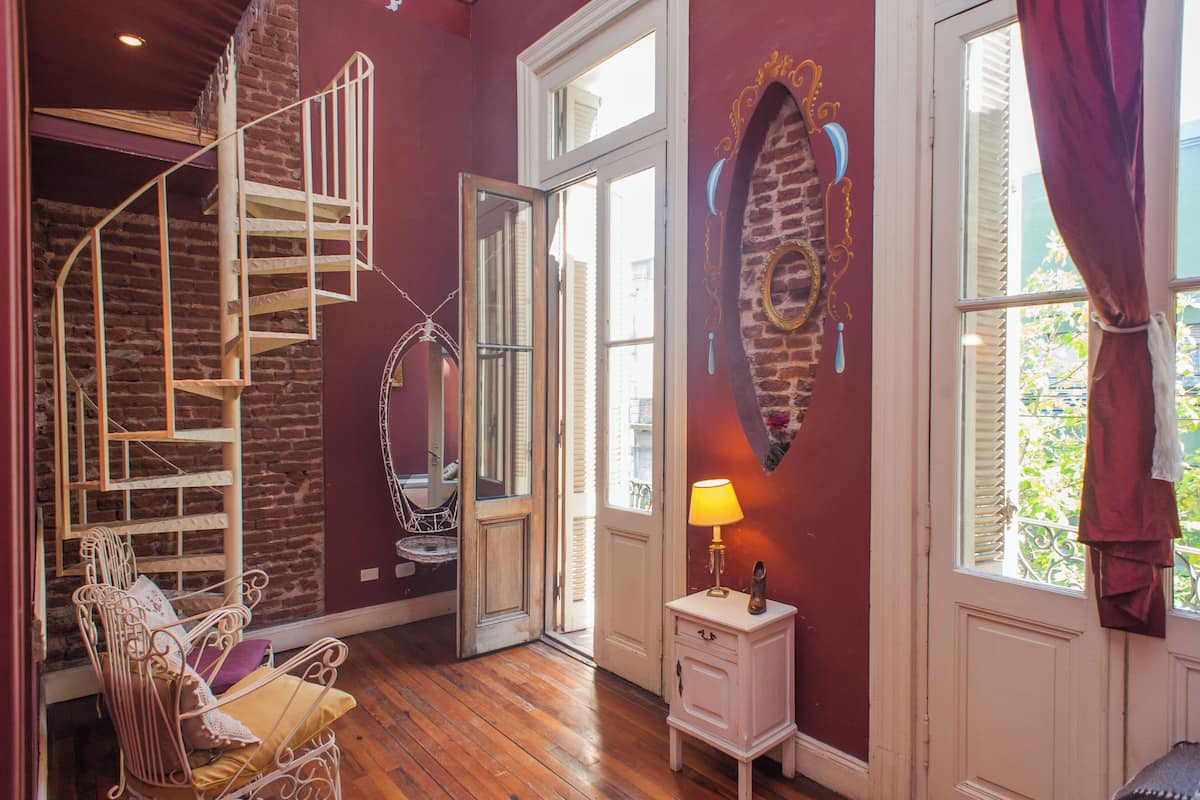 A room with a spiral staircase, a small table with a lamp, and a window with curtains.