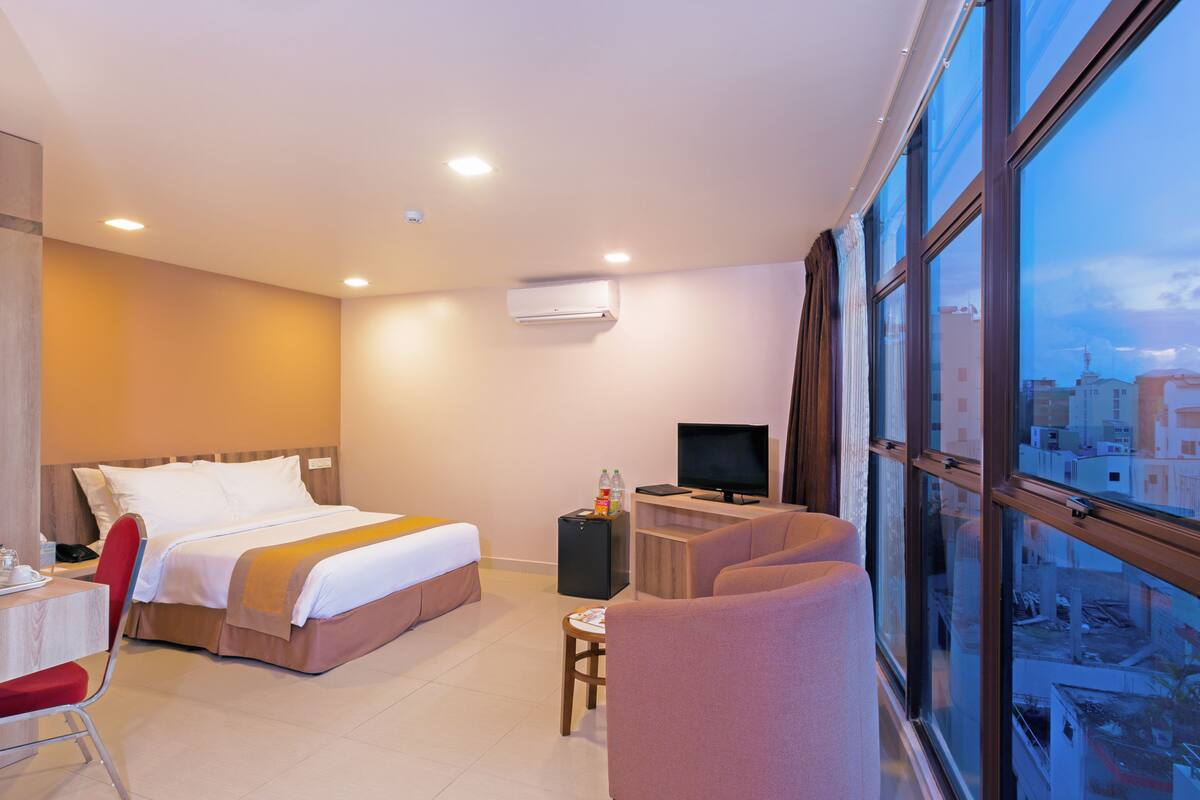 A hotel room with a bed, a desk, a chair, a television, and a window with a city view.
