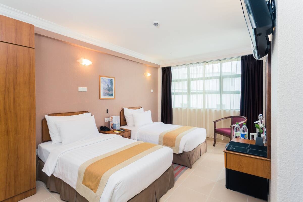 A hotel room with two beds, a desk with a computer, a chair, and a window with curtains.