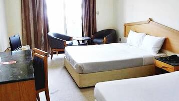 A hotel room with a bed, a desk, a chair, and a small table.
