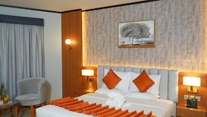 Ein Hotelzimmer mit einem großen Bett, zwei Nachttischen, einem Sessel und einem Bild an der Wand.