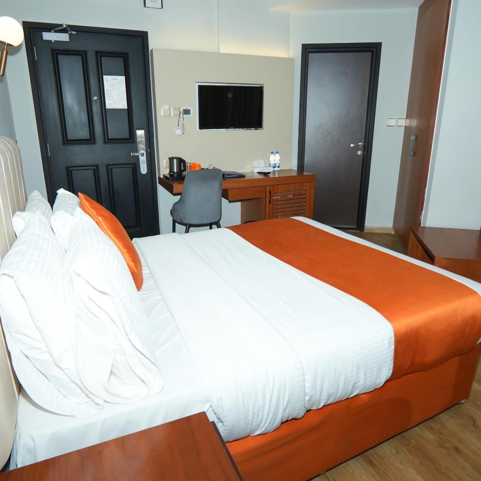 Una habitación de hotel con cama, escritorio, silla y televisor en la pared.