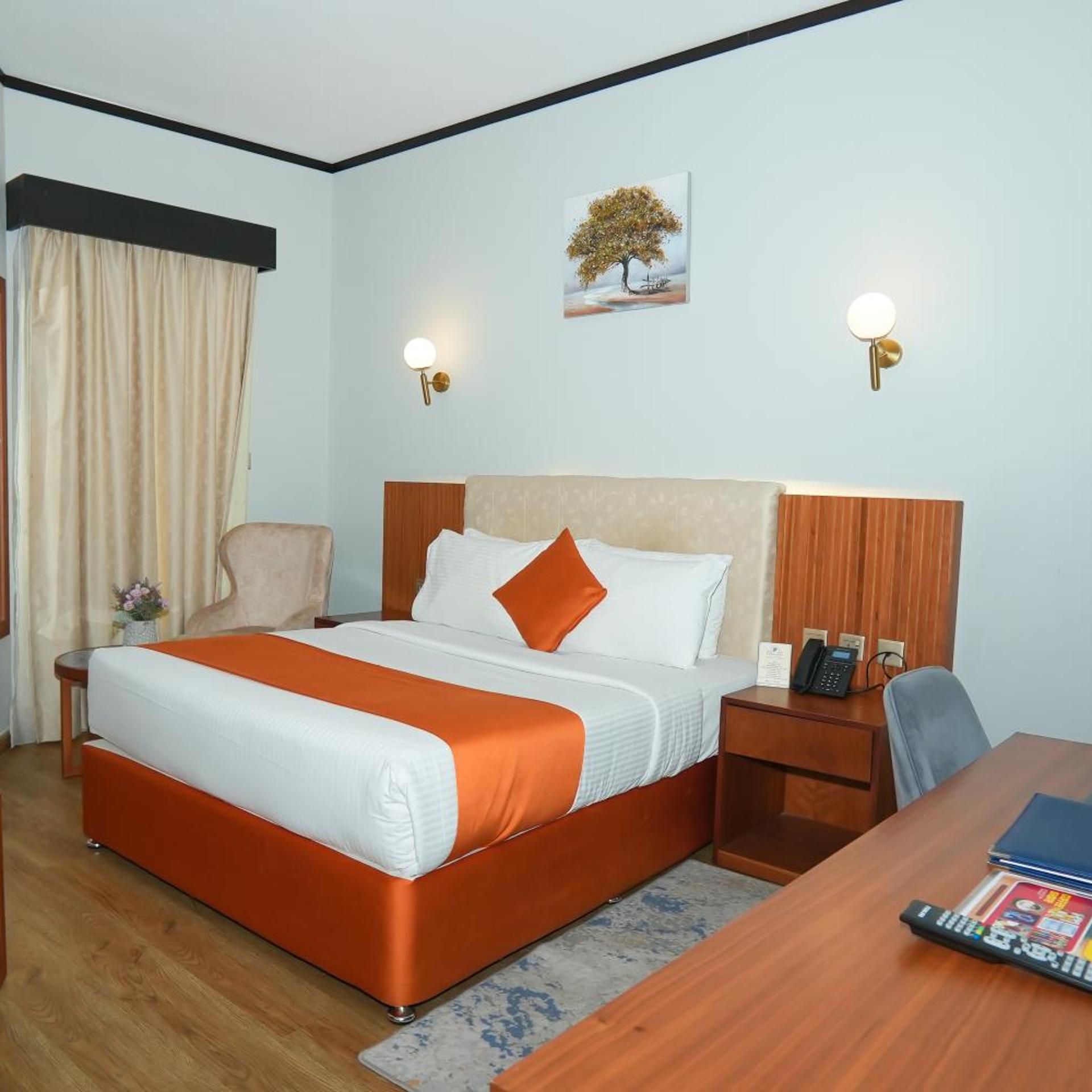 Una habitación de hotel con cama, escritorio, silla, mesita de noche y lámpara de pared.