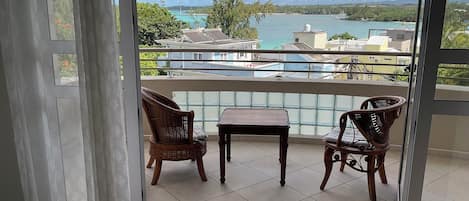 A balcony with two wicker chairs and a small table, overlooking a body of water and buildings.