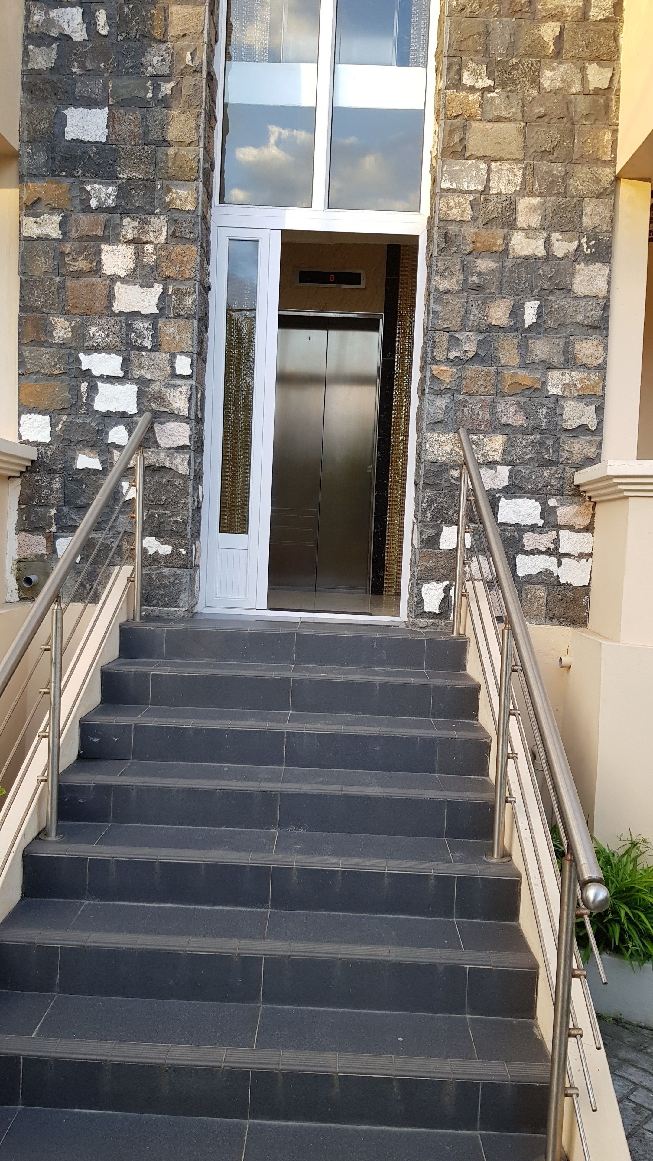 Una escalera que conduce a un ascensor en un edificio de paredes de piedra y una puerta blanca.