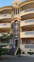 Un hotel de varios pisos con una entrada central flanqueada por pilares de piedra, varios balcones y una escalera que conduce a la entrada.