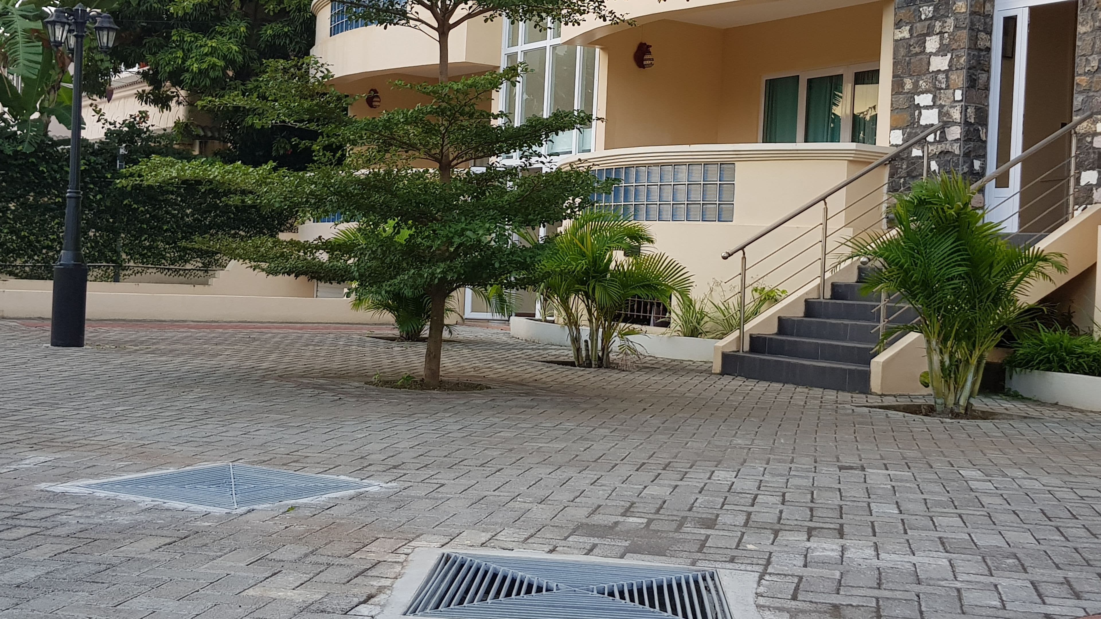 A paved courtyard with a staircase leading to a building with a beige facade and stone accents.
