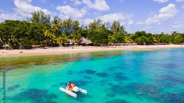 Mar turquesa transparente con un bote llevando dos personas. Palmeras y cabañas a lo largo de la playa.
