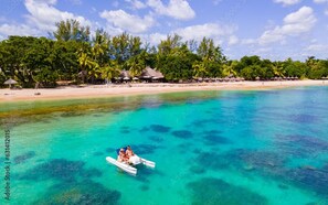 Mar turquesa transparente con un bote llevando dos personas. Palmeras y cabañas a lo largo de la playa.