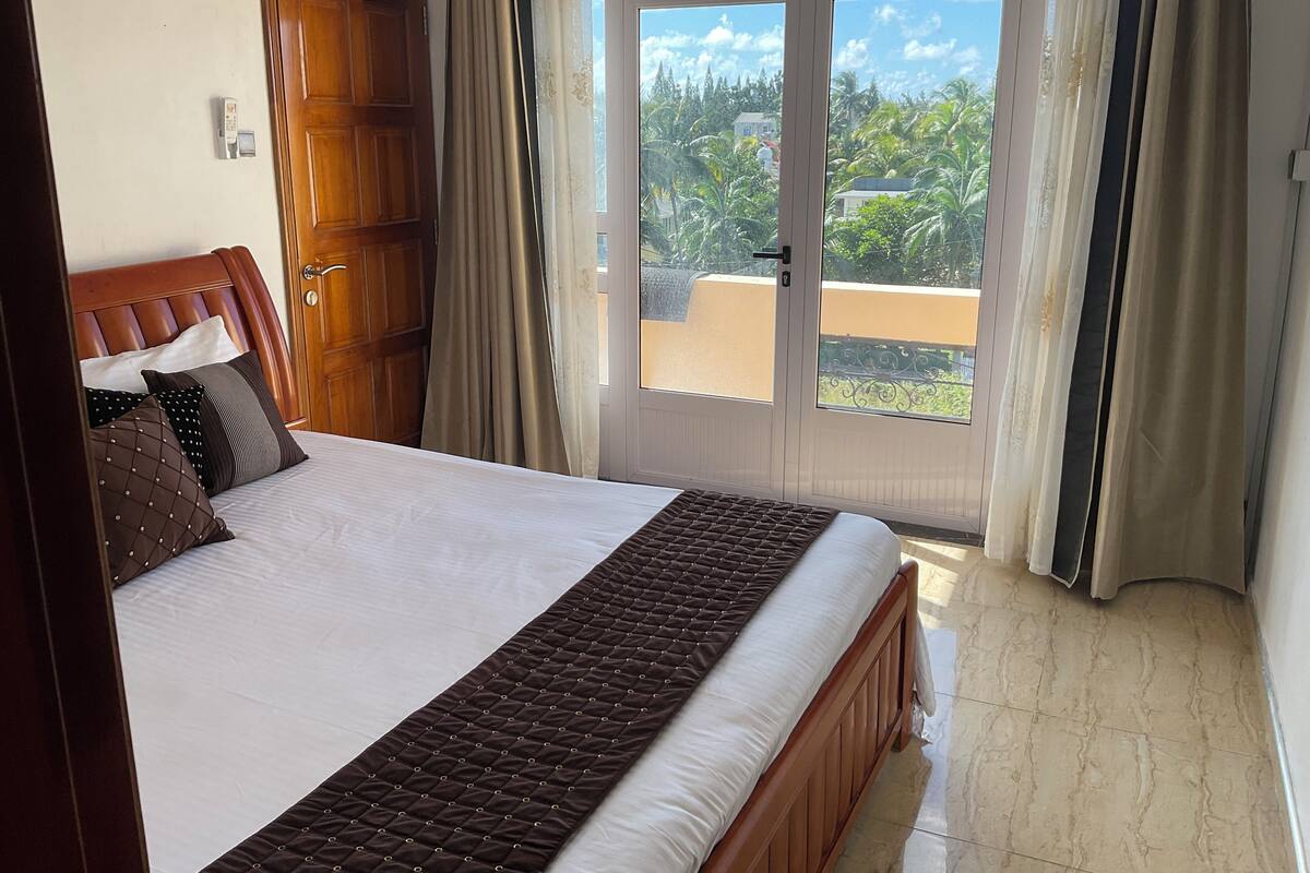A bedroom with a large bed, wooden headboard, and a view of greenery through the door.