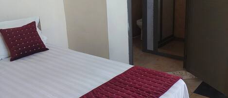 Un letto rifatto con una coperta bianca e rossa, un cuscino rosso e un interruttore a muro.