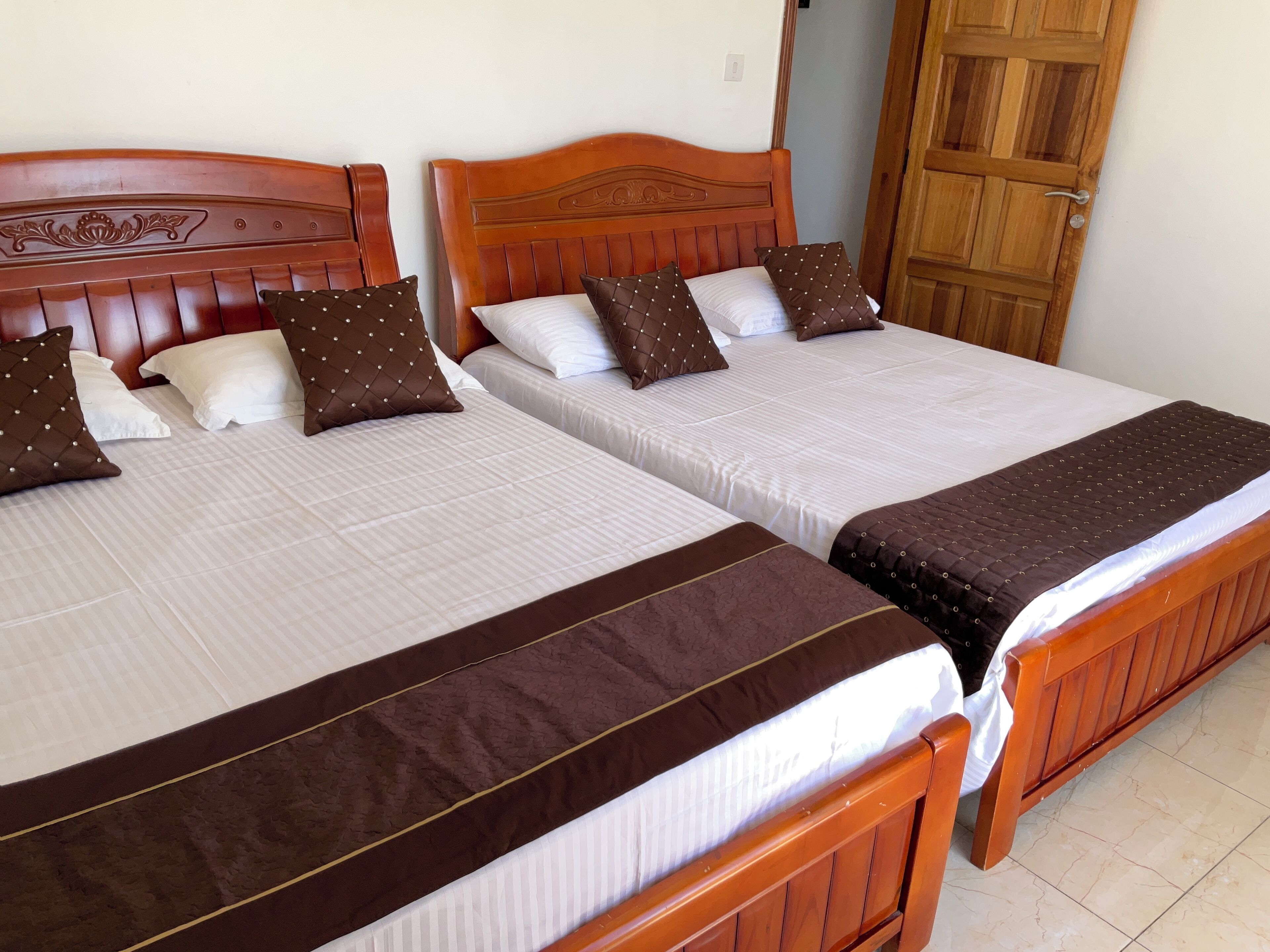 Dos camas de madera con cabeceras, ropa de cama blanca y almohadas decorativas marrones.