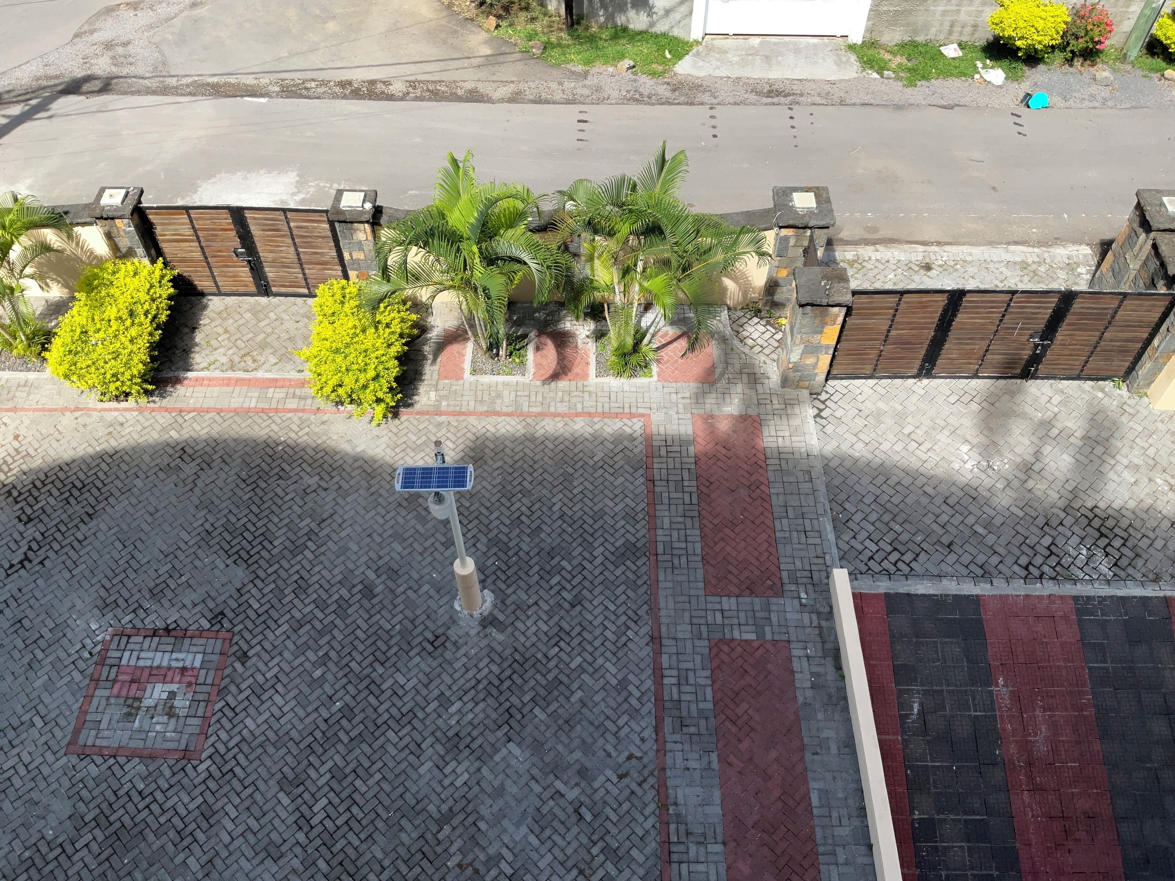 A paved area with a solar-powered streetlight, a metal fence, and green bushes.