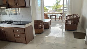 Una cocina moderna con una isla central, armarios de madera y un comedor con mobiliario de mimbre y vistas al exterior.