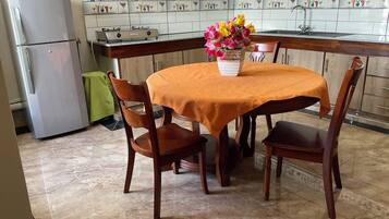 Una cocina con una mesa de comedor, sillas, un refrigerador, una estufa a gas y un salpicadero de azulejos.