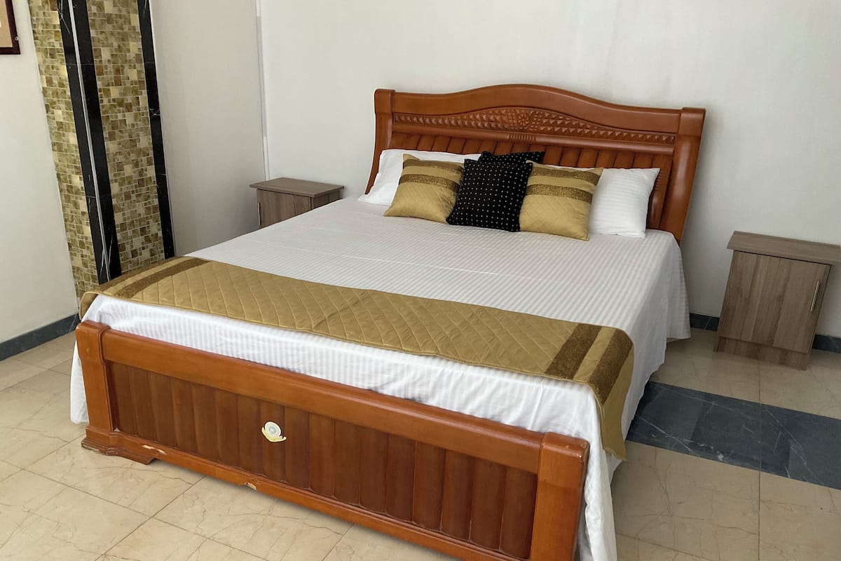 Uma cama grande com cabeceira de madeira, duas mesinhas de cabeceira e um edredom acolchoado.