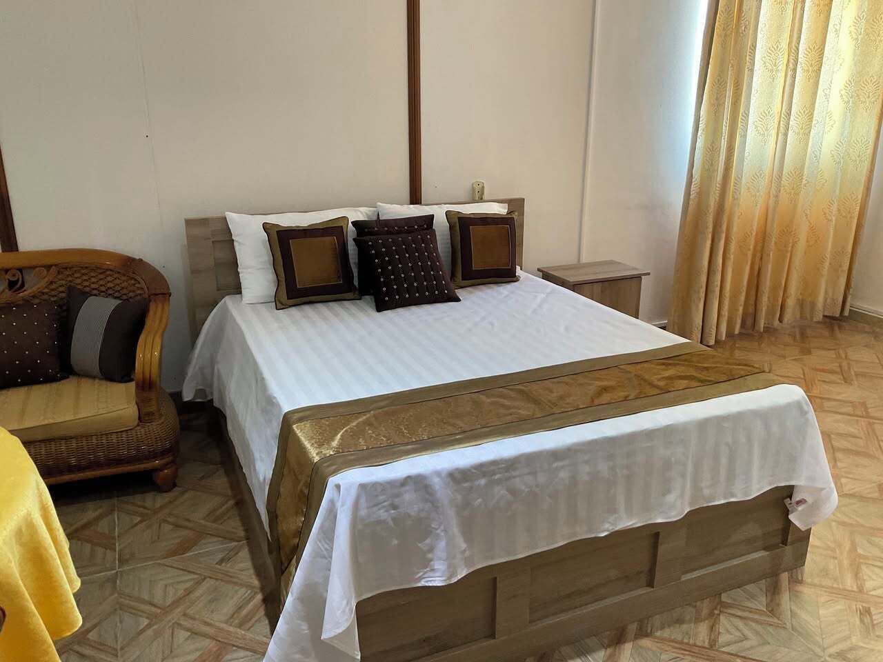 A neatly made bed with a white and gold bedspread, a wooden headboard, and a nightstand with a lamp.