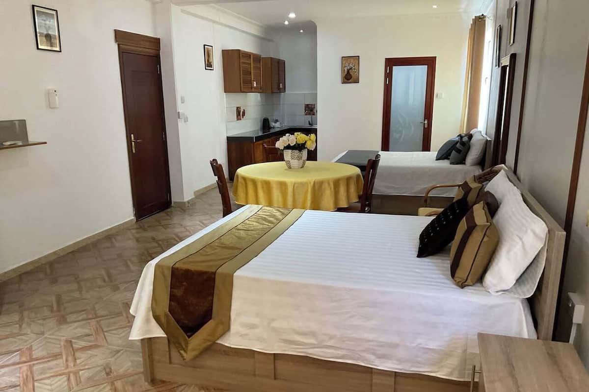 Quarto de hotel com cama, mesa pequena para refeições, cozinha e banheiro.