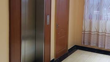 Un ascensor, una puerta de madera y una cortina estampada en un pasillo.