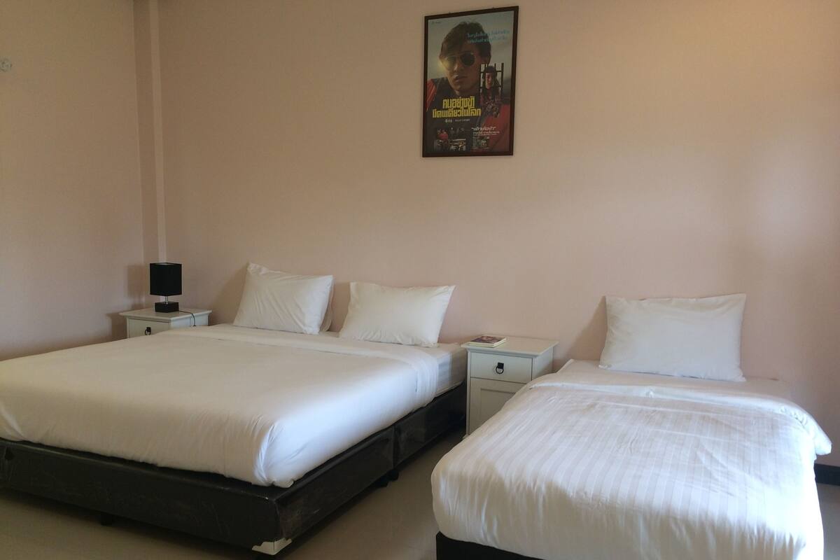A hotel room with two beds, white bedding, a nightstand with a lamp, and a poster on the wall.