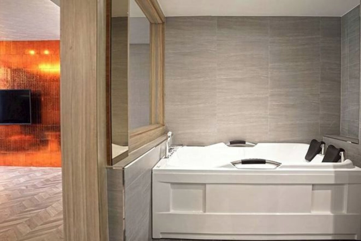 A modern bathroom with a large bathtub, a mirror, and a wooden floor.