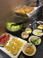 Un buffet con diversi cibi, tra cui anguria, fettine di limone, pannocchie e una ciotola di insalata.